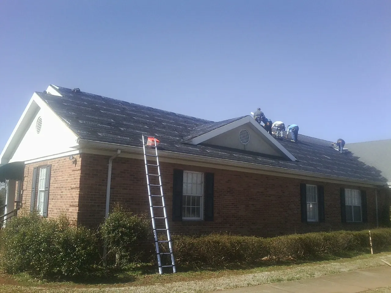Crew tearing shingles off a brick ranch roof with a ladder set — Emergency Roof Repair work by our crew in Grant
