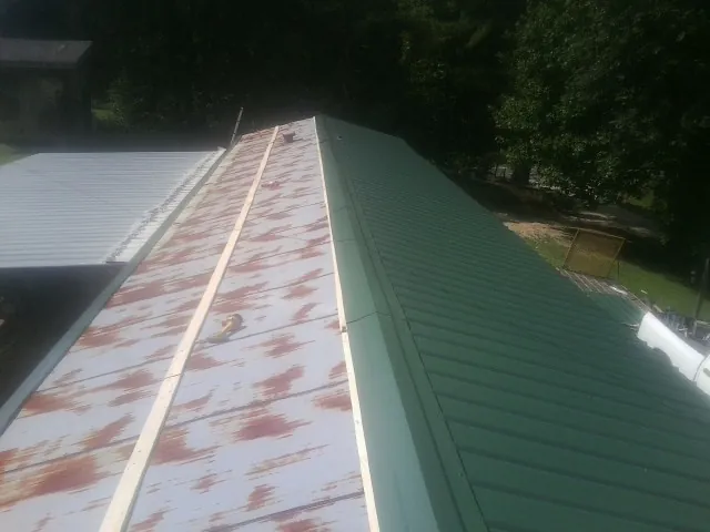 Old rusted panels beside newly installed green metal roofing — Wind Damage Roof Repair by Roofing Brothers in Grant